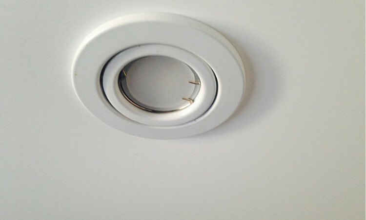 Spot encastré rond blanc avec anneau chromé installé dans un faux plafond tendu blanc