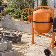Bétonnière électrique orange sur un chantier de maçonnerie, artisan montant un muret en parpaings
